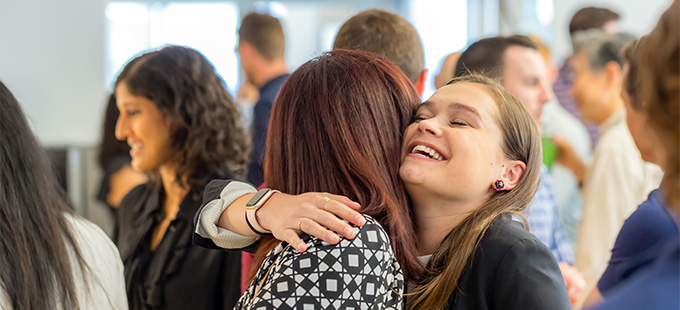 Happy woman hugging a coworker in a busy office