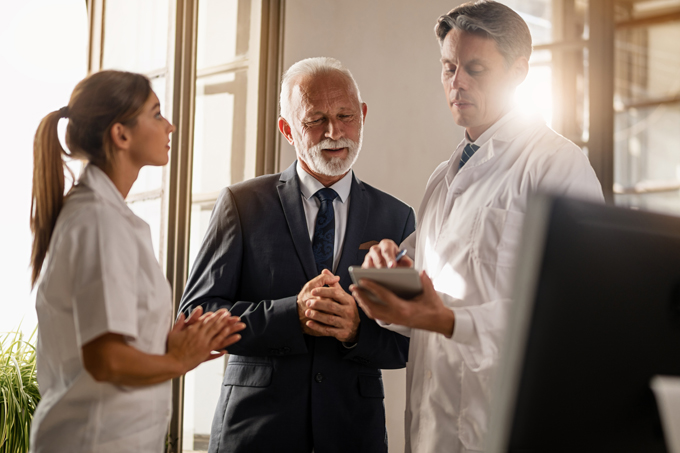 Mature businessman and male doctor working on digital tablet at medical clinic.